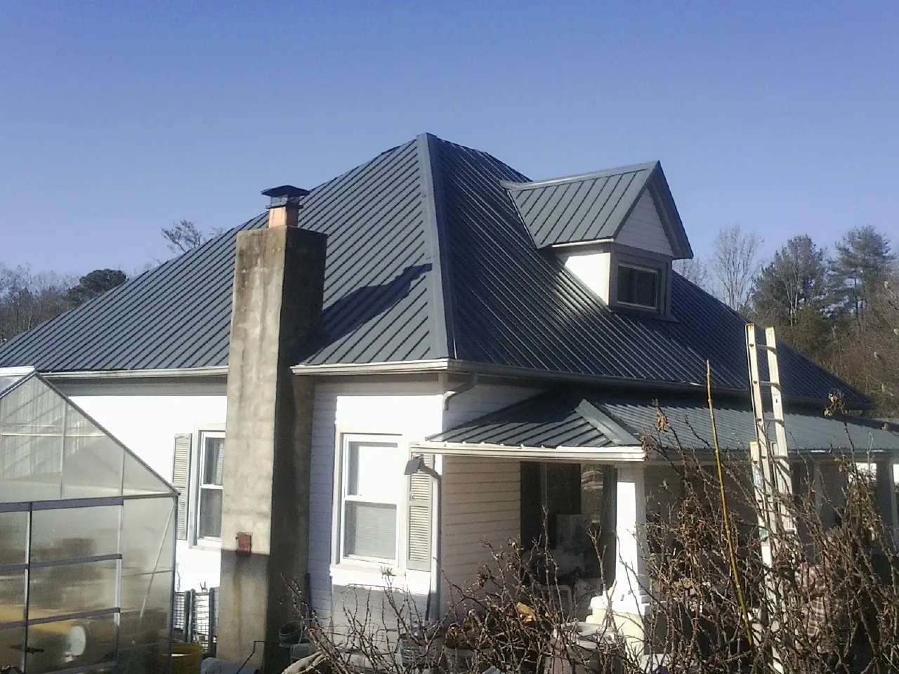 Dark blue standing seam metal roof on a white farmhouse with dormer in Jonesville