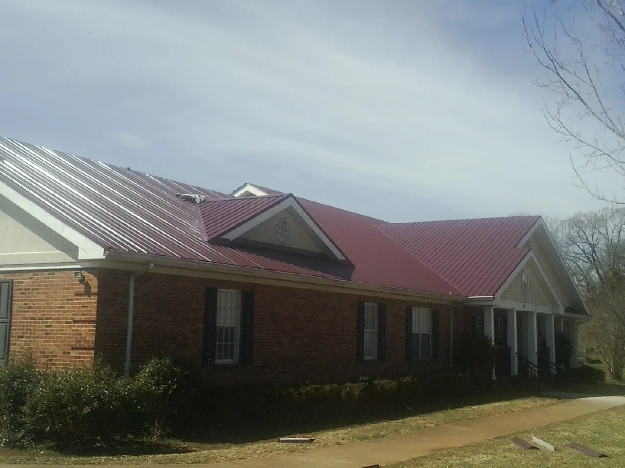 Red metal roof with gabled entries on a long brick building, from a Hail Damage Roof Repair job in Jonesville