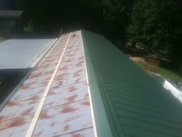Old rusted panels beside newly installed green metal roofing — Wind Damage Roof Repair by Roofing Brothers in Jonesville