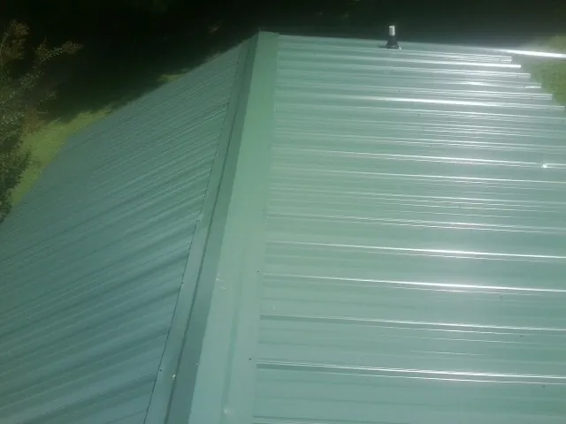 New green metal panels meeting at the ridge of a roof — Flat Roof Repair work by our crew in Jonesville