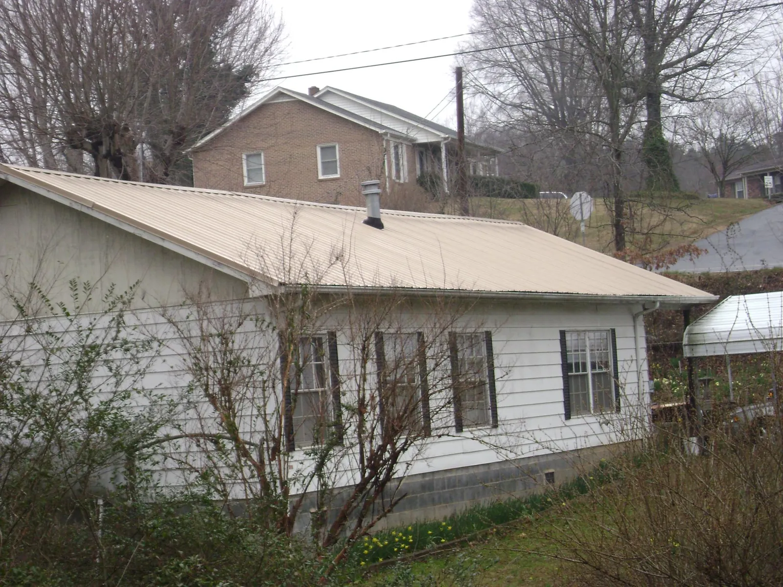 Tan metal roof on a white sided house set into a hillside — Commercial Roofing by Roofing Brothers in Jonesville